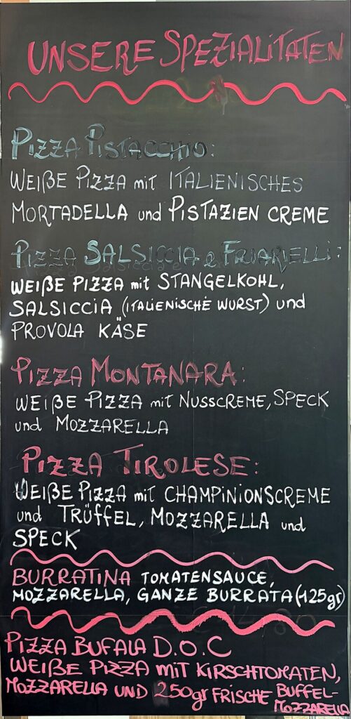Kreidetafel „Unsere Spezialitäten“ mit Pizza Pistacchio, Salsiccia e Friarielli, Montanara, Tirolese, Burratina und Bufala D.O.C.